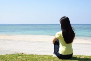 青い海を眺めながら芝生に座る女性の後ろ姿