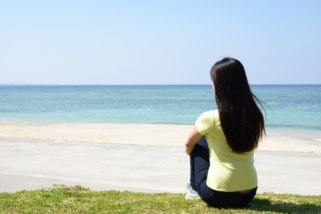 青い海を眺めながら芝生に座る女性の後ろ姿
