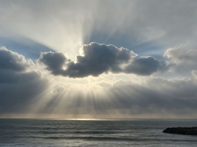 海上の厚い雲の隙間から降り注ぐ神秘的な光芒