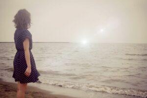 夕暮れの海辺に立ち水平線を見つめる女性
